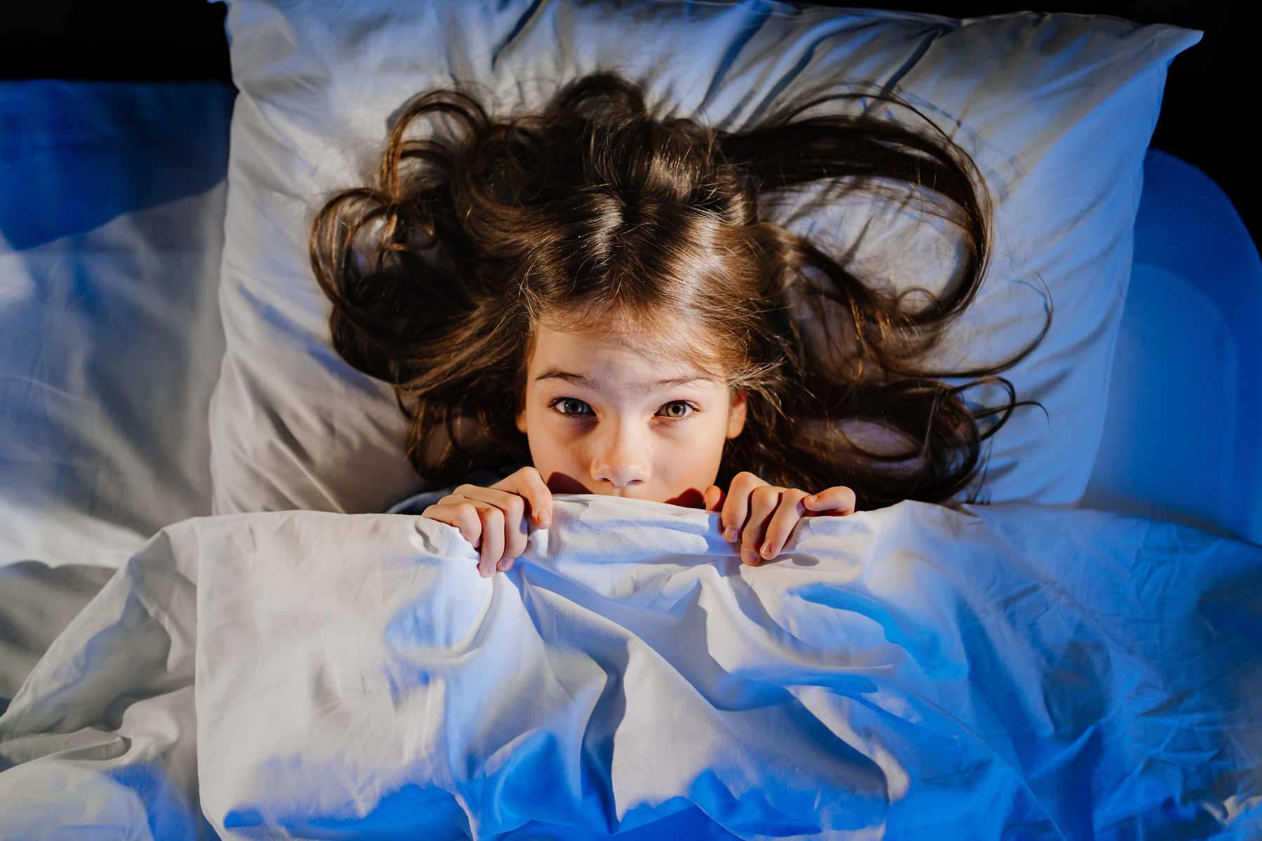 frightened girl covers his face with a blanket in bed in her room. child's fear